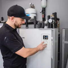 Technik w czapce z daszkiem obsługuje panel sterowania pompy ciepła NIBE.
