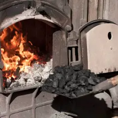 Fachowiec od pieca zasypuje węglem palenisko, gdzie szaleje ogień.