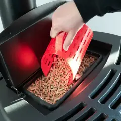 Ręka wsypuje pellet do zasobnika czarnego pieca na pellet.