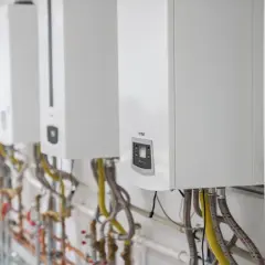 Rząd białych kotłów gazowych Termet, gotowych do montażu, z widocznymi przyłączami hydraulicznymi i gazowymi.