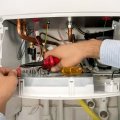 Serwisant De Dietrich naprawia kocioł, pracując przy przewodach i elementach elektronicznych.