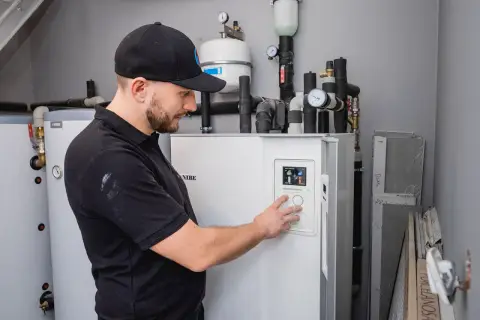 Technik w czapce z daszkiem obsługuje panel sterowania pompy ciepła NIBE.