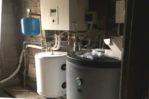 Instalacja pompy ciepła w starym domu: dwa zasobniki, niebieski zbiornik przeponowy i panel sterowania.