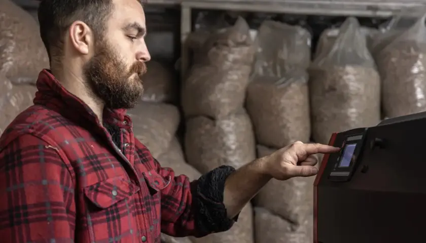 Mężczyzna w kratę reguluje panel sterowania kotła na pellet. To przykład modulacji kotła, czyli dostosowania jego pracy do potrzeb.