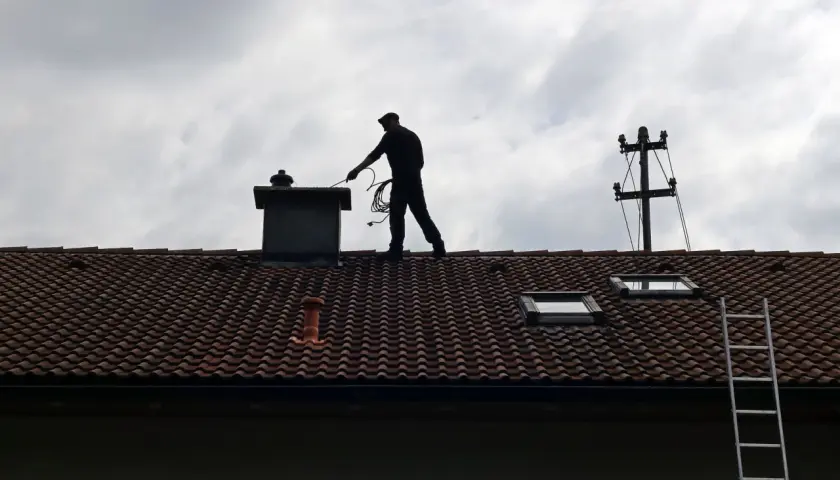 Kominiarz na dachu przygotowuje się do pracy. Zastanawiasz się, ile kosztuje szlamowanie komina?