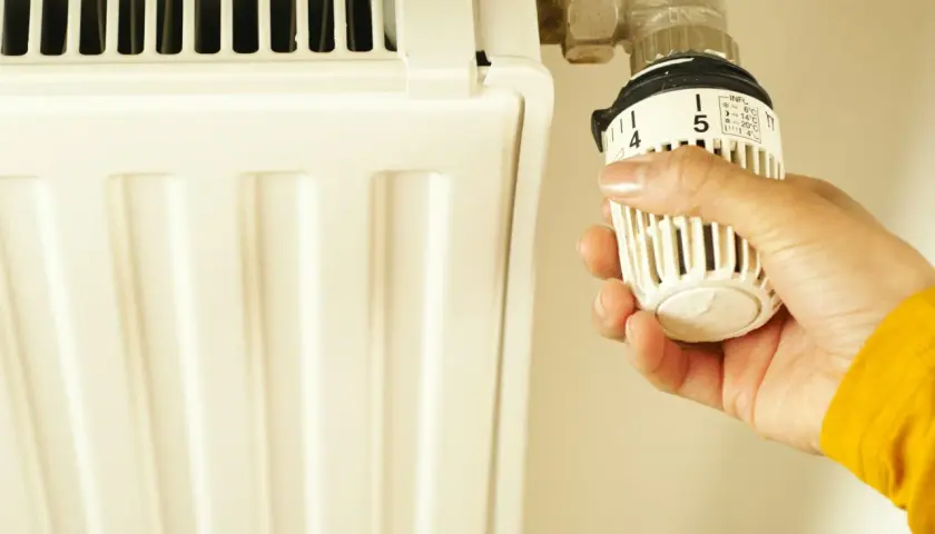 Dłoń reguluje termostat grzejnika. Czy piec gazowy powinien chodzić cały czas? Ustawienie 5 oznacza 20°C.