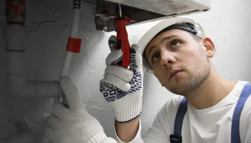 Instalator w rękawicach i kasku używa klucza do regulacji zaworu. Prawdopodobnie przygotowuje środek do płukania instalacji CO.