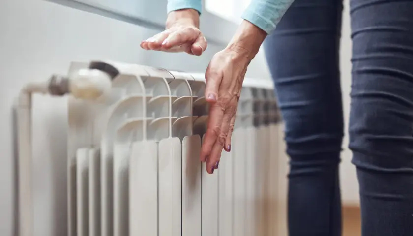 Dłoń sprawdza temperaturę grzejnika, który nie grzeje na dole.