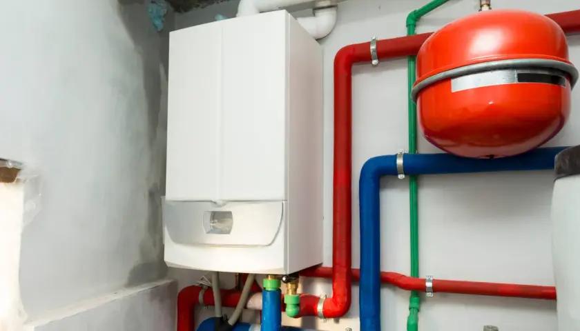 Biały piec gazowy podłączenie do instalacji grzewczej z czerwonymi i niebieskimi rurami oraz czerwonym zasobnikiem.