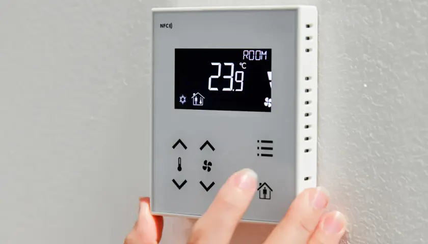 Dłoń reguluje termostat, pokazując jak ustawić temperaturę na pompie ciepła. Aktualna temperatura to 23.9°C.