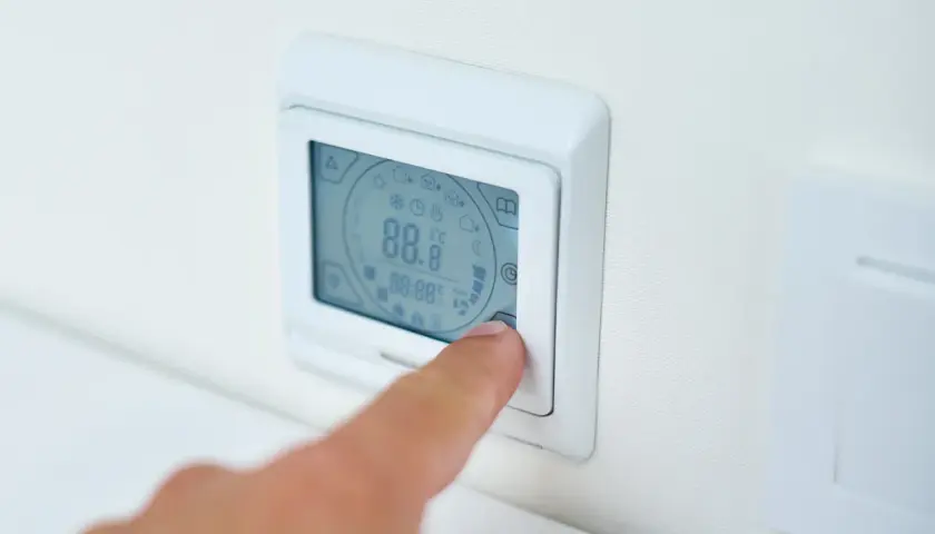 Palec naciska przycisk termostatu, ustawiając idealną temperaturę pieca gazowego.