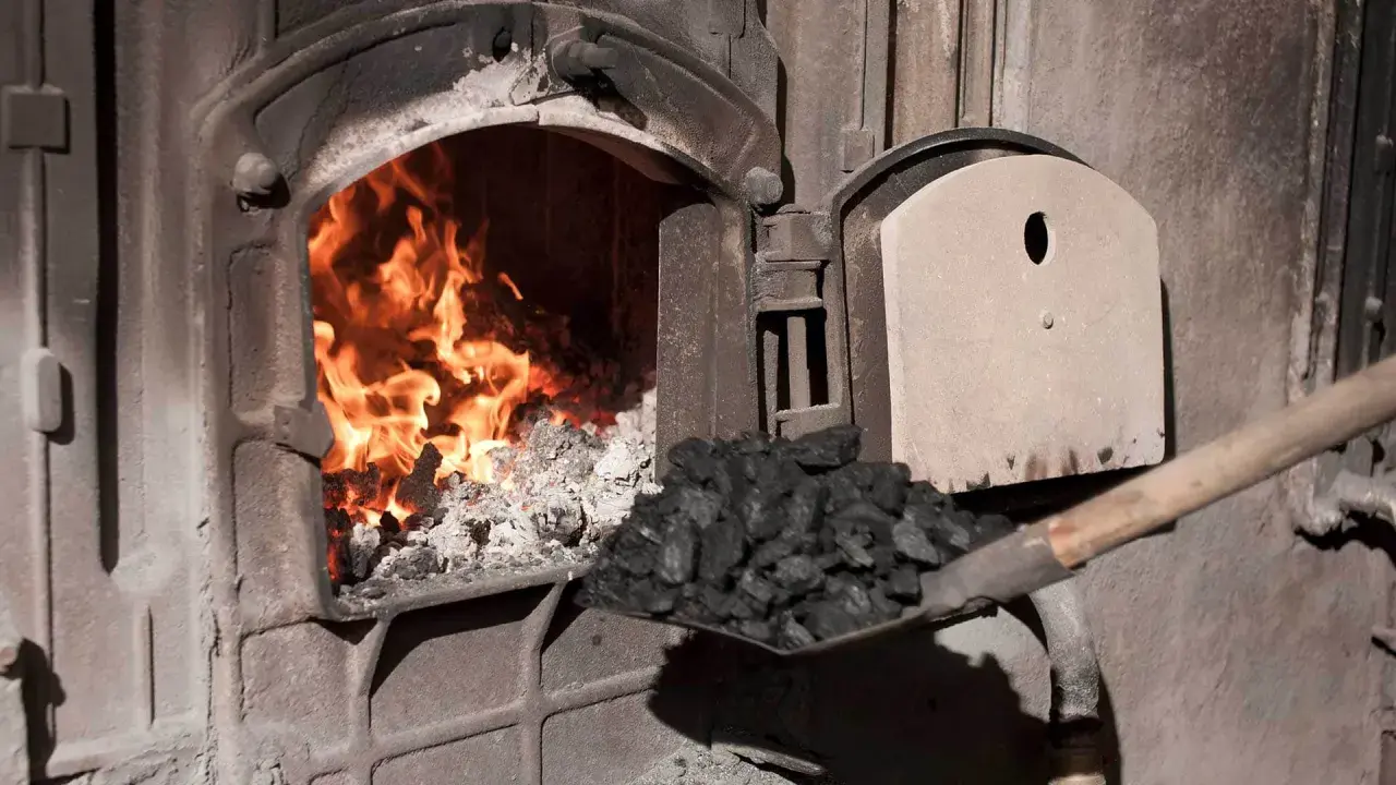 Fachowiec od pieca zasypuje węglem palenisko, gdzie szaleje ogień.
