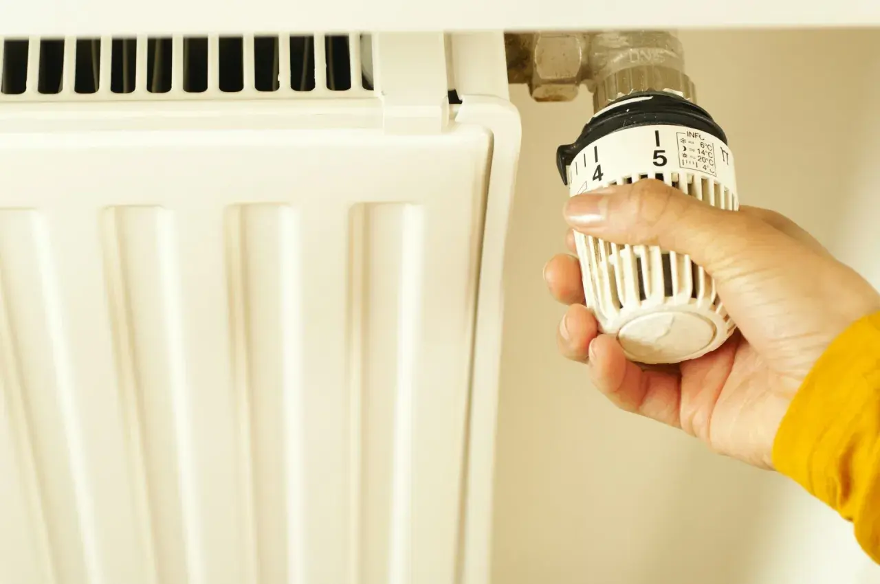Dłoń reguluje termostat grzejnika. Czy piec gazowy powinien chodzić cały czas? Ustawienie 5 oznacza 20°C.