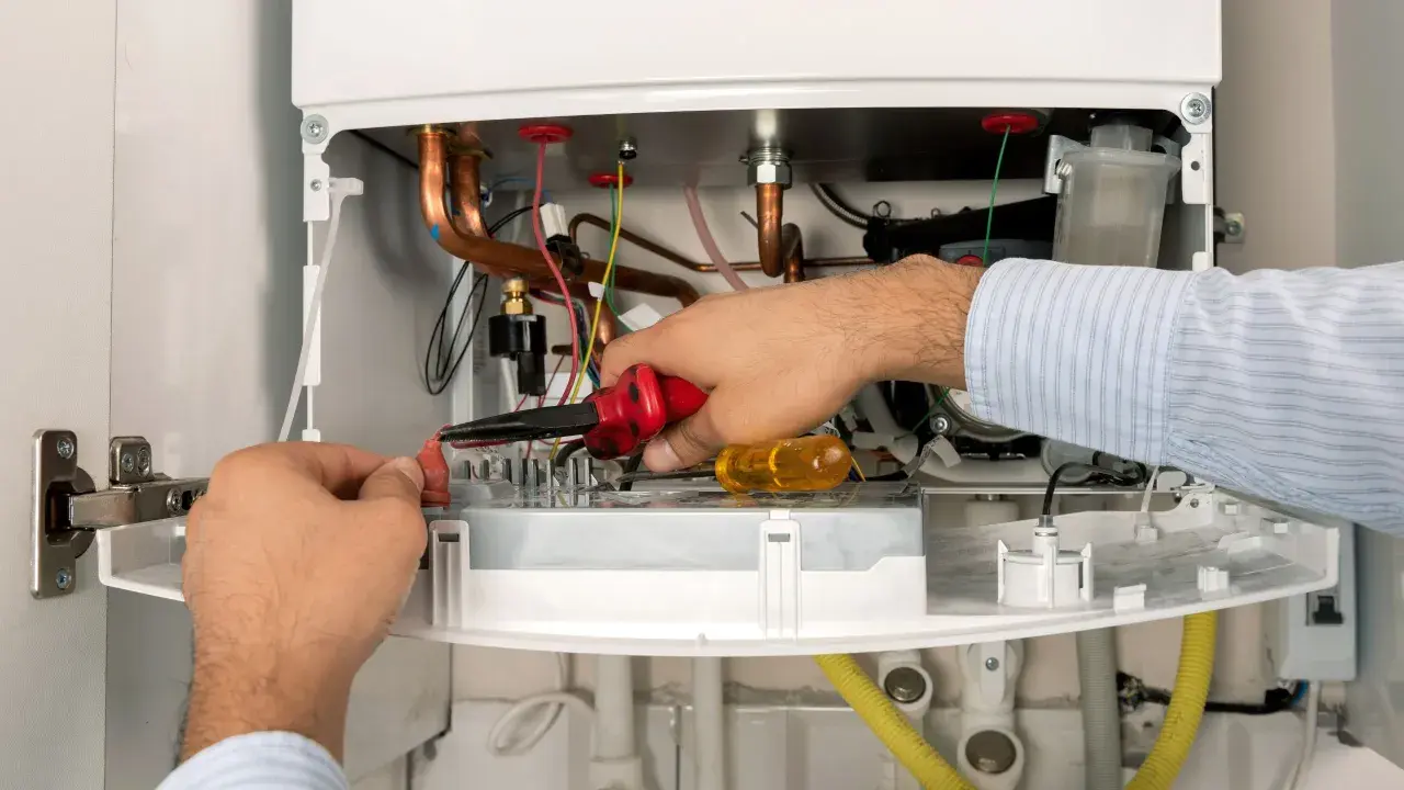 Serwisant De Dietrich naprawia kocioł, pracując przy przewodach i elementach elektronicznych.