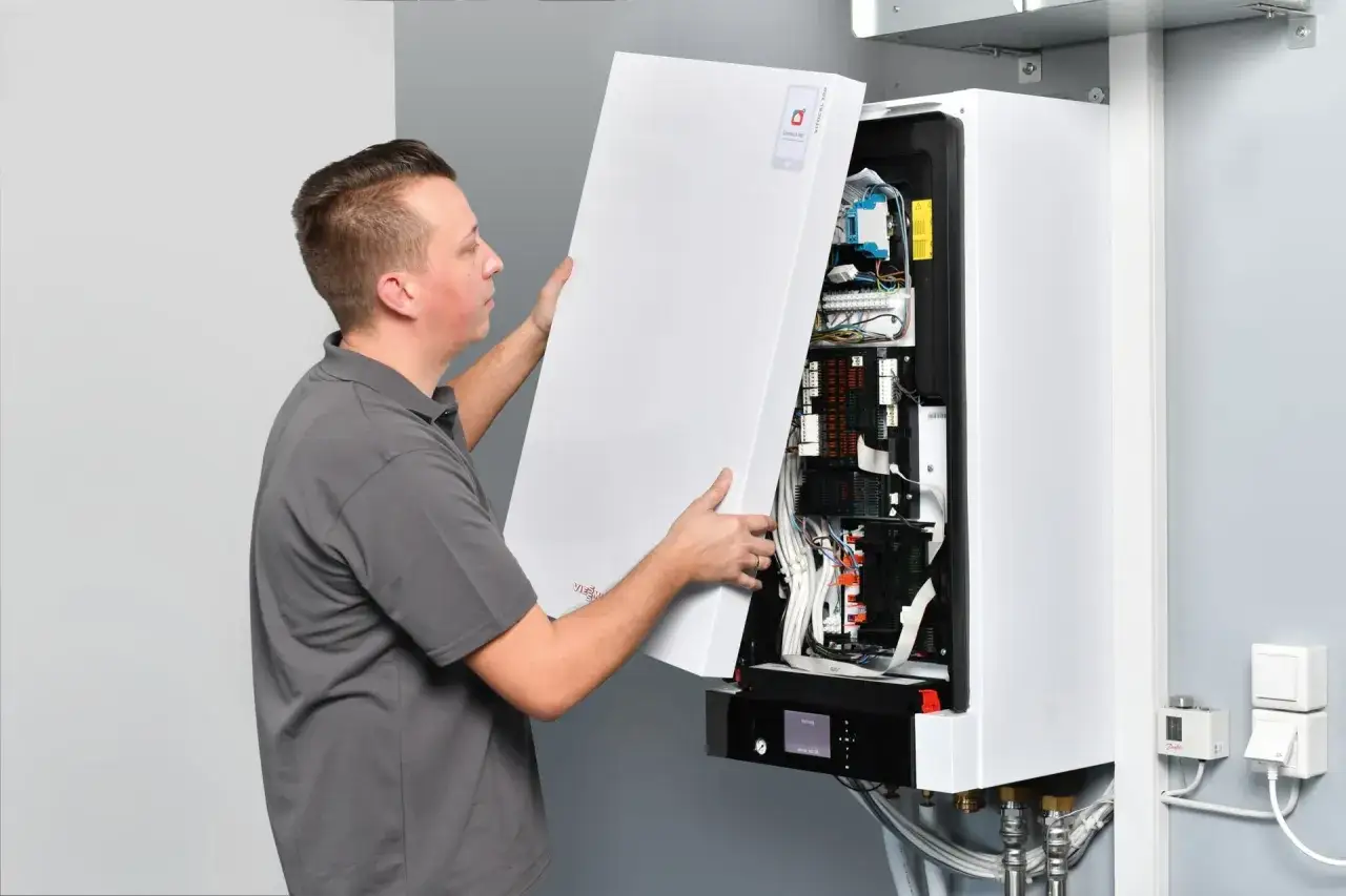 Technik montuje obudowę pieca gazowego. Trwa pierwsze uruchomienie pieca gazowego, widoczne są przewody i elektronika.