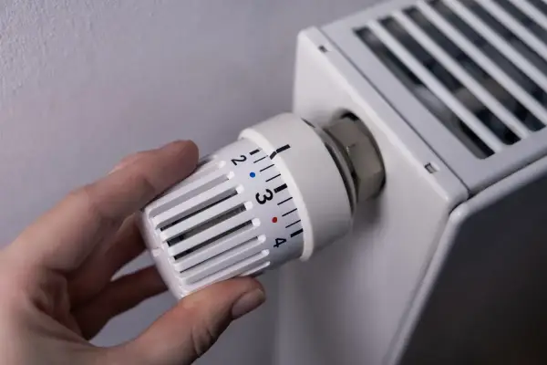 Dłoń reguluje termostat grzejnika, kontrolując ogrzewanie domu na gaz. Ustawienie temperatury na 3.